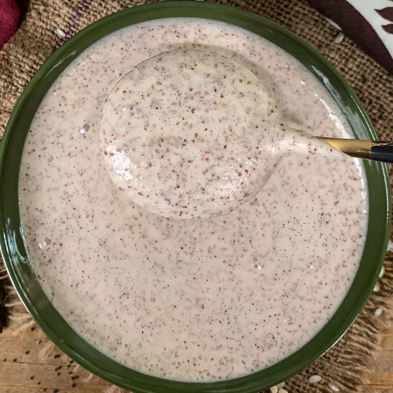 A green bowl filled with creamy, speckled Indian batter, with a ladle scooping some out.