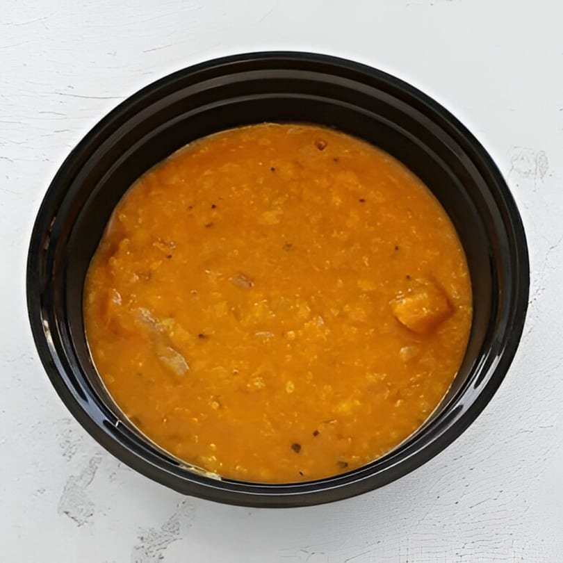 A black bowl filled with orange Indian dal, featuring visible lentils and spices.